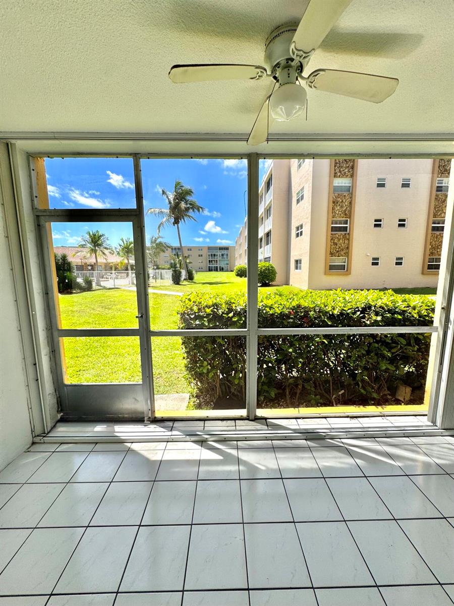 A tiled sunroom features a ceiling fan and a screened view of a grassy courtyard — 202 SE 10th Street # 105, Dania Beach FL 33004, DANIA BEACH, FL