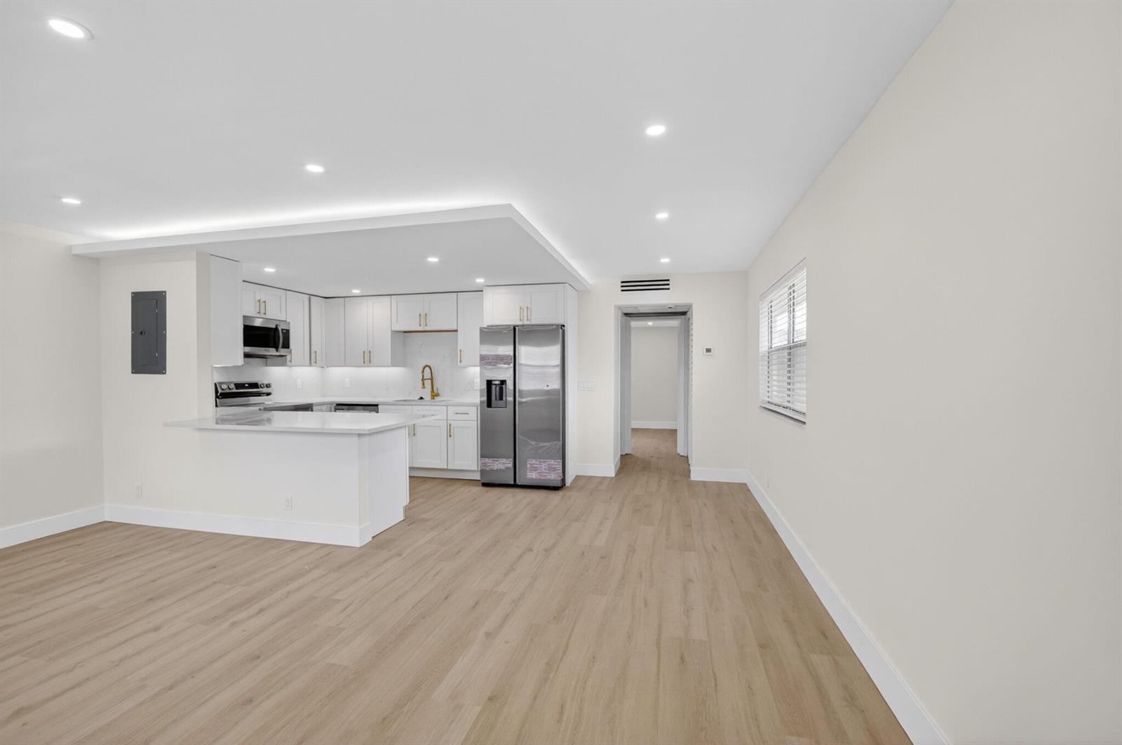 A modern kitchen with white cabinets and stainless steel appliances opens to a living area — 270 Brittany F, Delray Beach FL 33446, DELRAY BEACH, FL