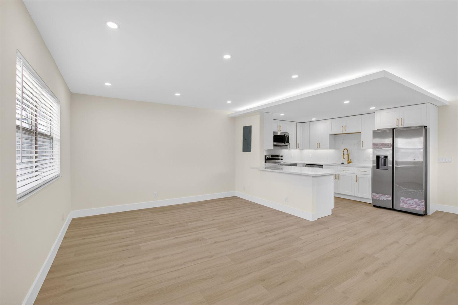 An open-concept kitchen with white cabinets and stainless steel appliances overlooks a spacious living area — 270 Brittany F, Delray Beach FL 33446, DELRAY BEACH, FL