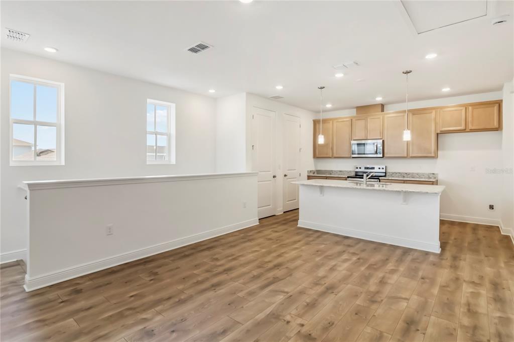 A kitchen with light wood cabinets and a white island overlooks an open living area — 10388 BRAGG ALLEY, ORLANDO, FL