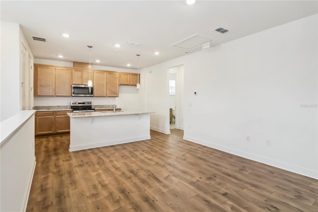 An open-concept kitchen features light wood cabinets, granite countertops, and wood-look flooring — 10388 BRAGG ALLEY, ORLANDO, FL