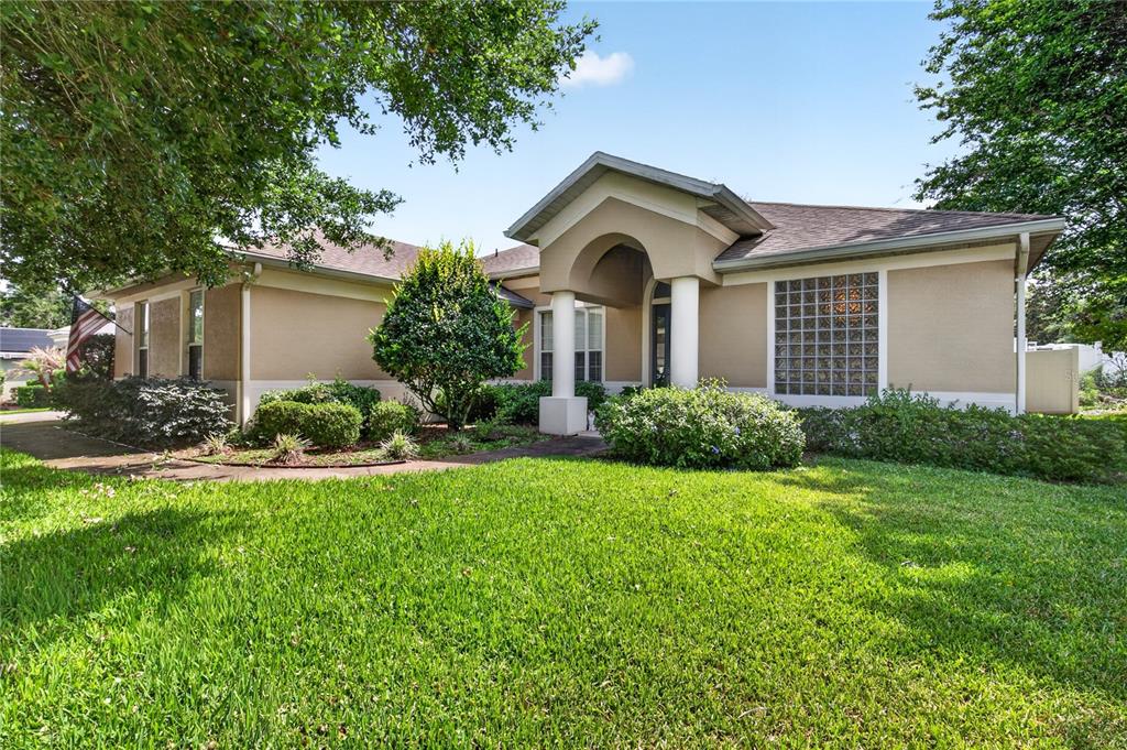 A single-story house with a tan stucco exterior, arched entryway, and glass block window — 36806 WINFIELD COURT, GRAND ISLAND, FL