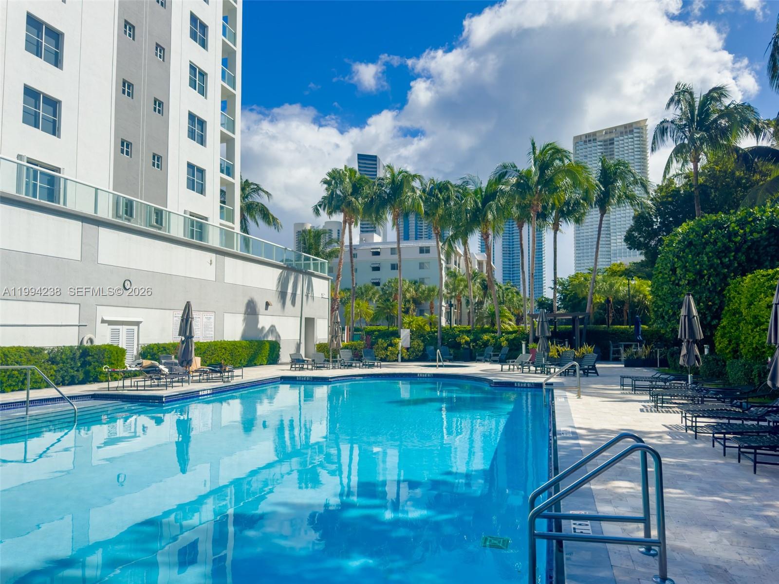 A swimming pool sits on a paved deck surrounded by palm trees and apartment buildings — SUNNY ISLES BEACH, FL