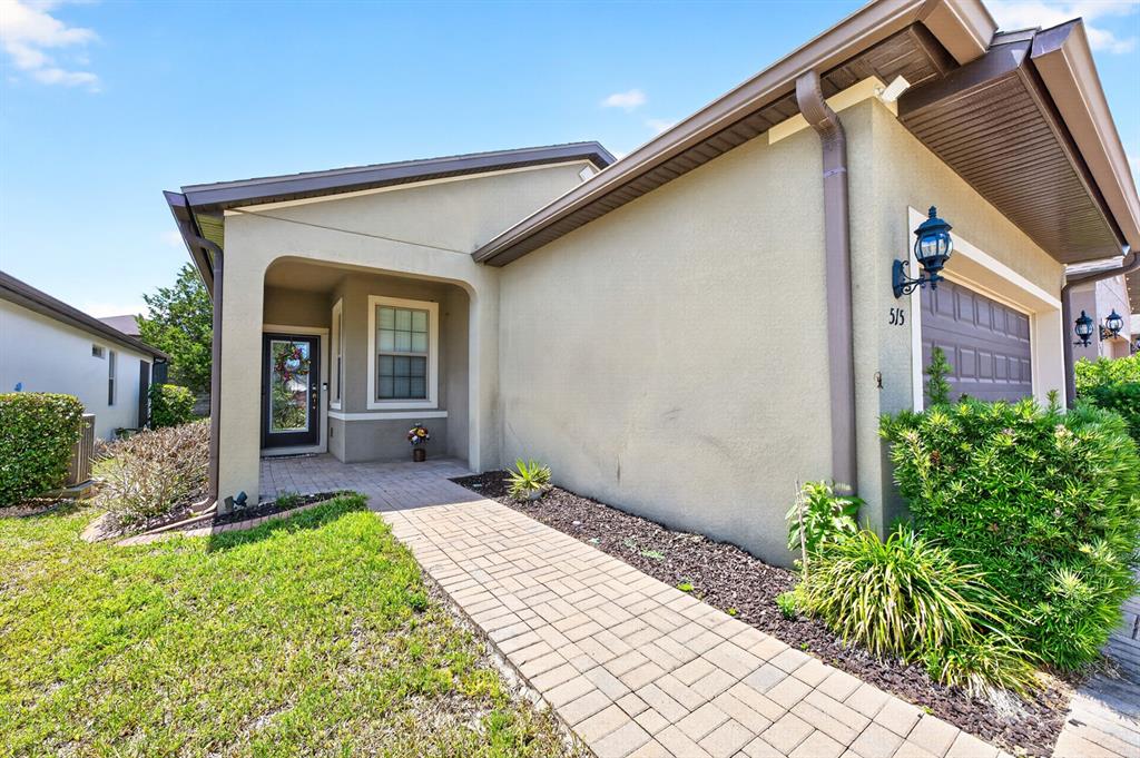 A paved walkway leads to the front entrance of a beige house with a garage — 515 PAMPLONA PLACE, DAVENPORT, FL