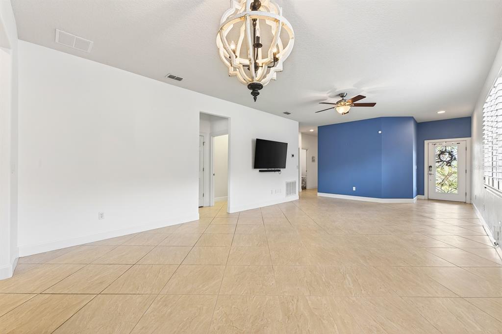 A living room features light tile flooring, a large chandelier, a ceiling fan, and blue walls — 515 PAMPLONA PLACE, DAVENPORT, FL