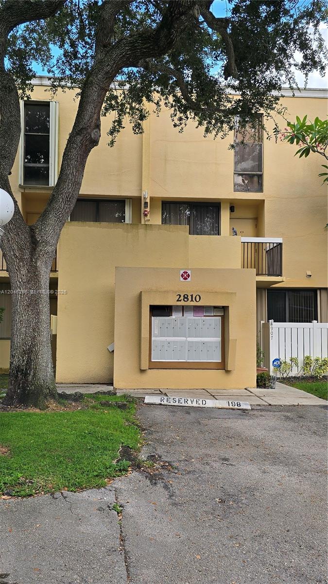 A yellow multi-story building features a central outdoor mailbox kiosk and a reserved parking space — 2810 SW 87th Ave # 910, Davie FL 33328, DAVIE, FL