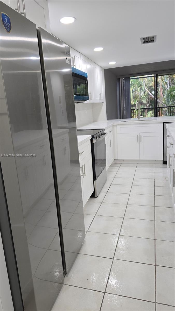 A modern kitchen features white cabinets, stainless steel appliances, and light-colored tile flooring — 2810 SW 87th Ave # 910, Davie FL 33328, DAVIE, FL