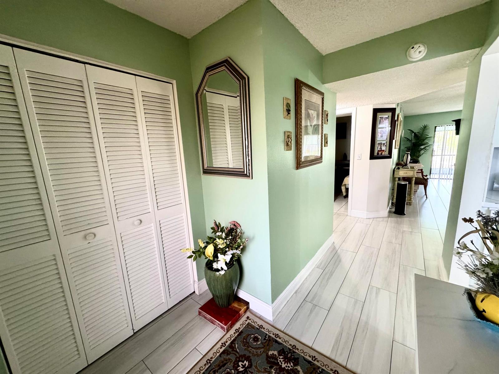 A hallway with light green walls, white louvered closet doors, and light-colored wood-look tile flooring — 4930 E Sabal Palm Boulevard # 107, Tamarac FL 33319, TAMARAC, FL
