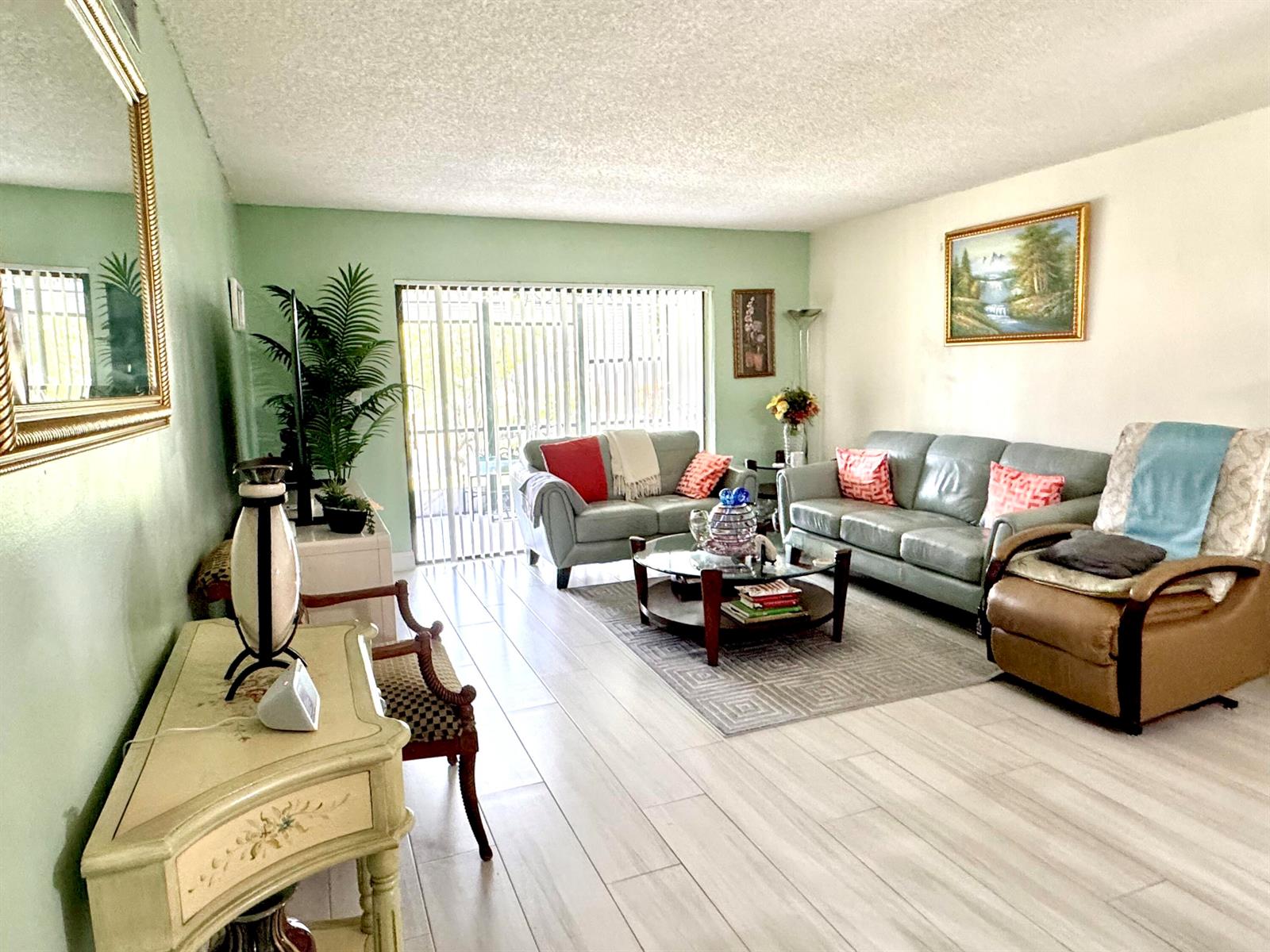A living room features light green walls, wood-look tile flooring, and a sliding glass door — 4930 E Sabal Palm Boulevard # 107, Tamarac FL 33319, TAMARAC, FL