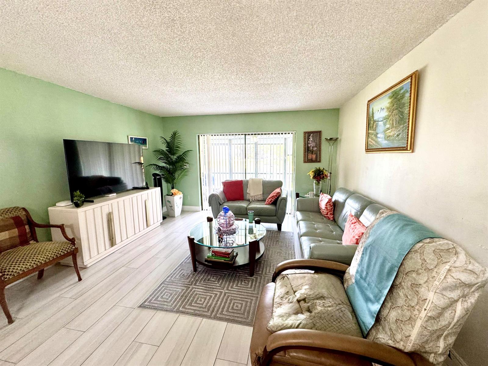 A living room features light green walls, a glass coffee table, and a leather sofa — 4930 E Sabal Palm Boulevard # 107, Tamarac FL 33319, TAMARAC, FL