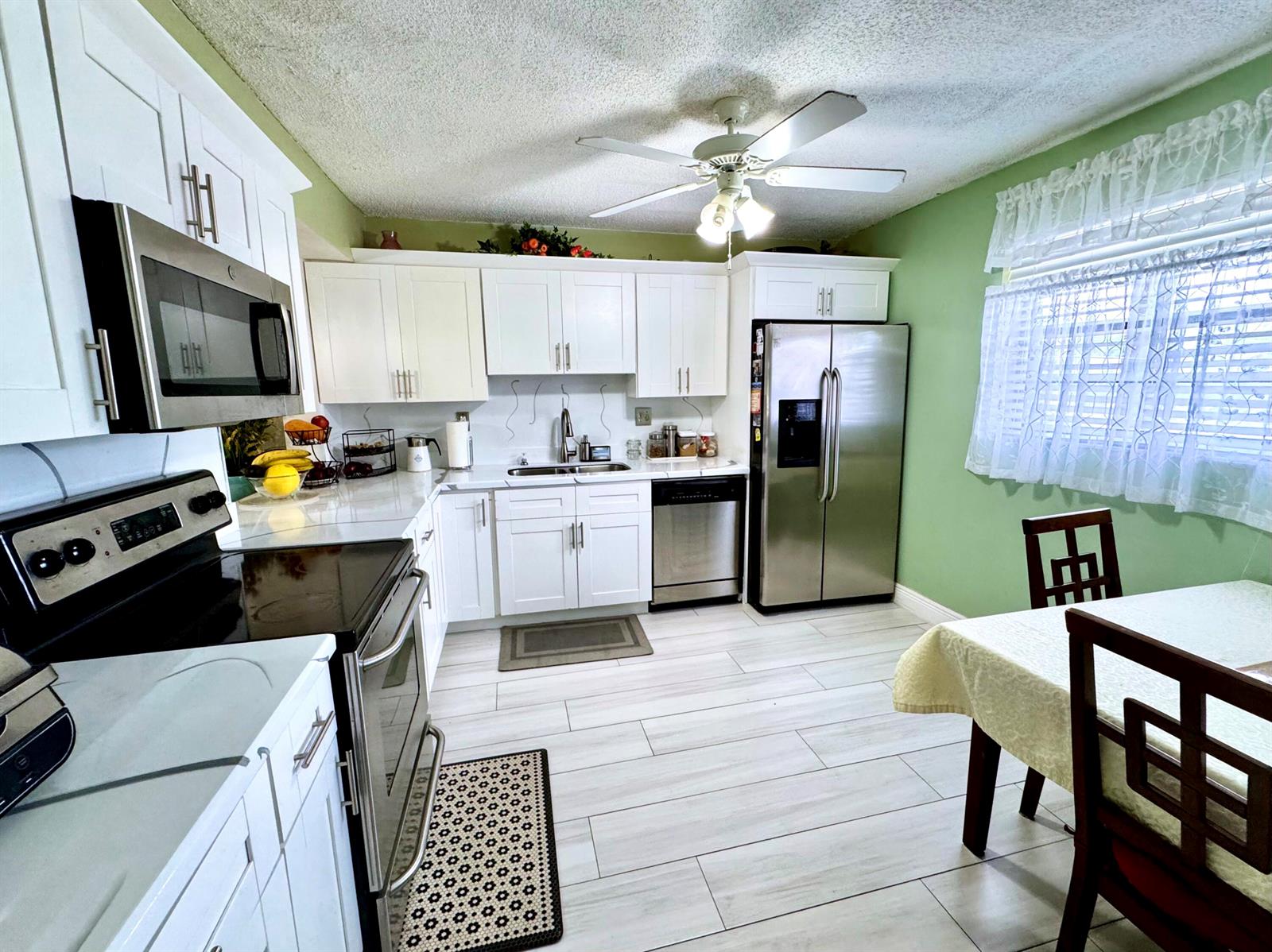 A kitchen features white cabinets, stainless steel appliances, green walls, and light-colored tile flooring — 4930 E Sabal Palm Boulevard # 107, Tamarac FL 33319, TAMARAC, FL