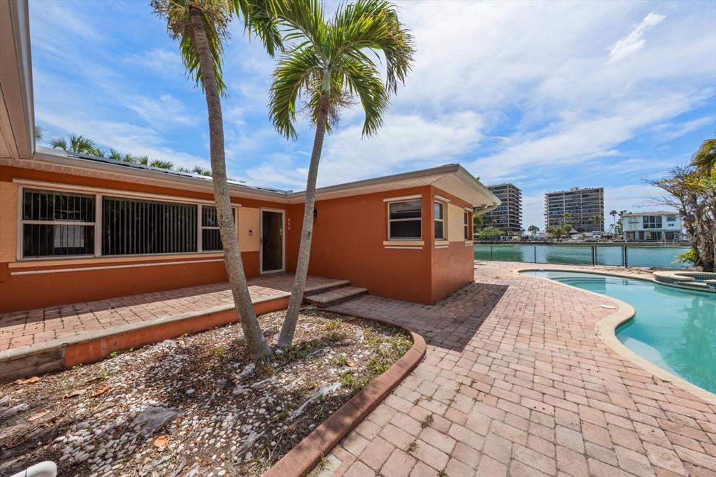 An orange house exterior with a patio, swimming pool, and palm trees by the water — 630-650 79TH AVENUE, ST PETE BEACH, FL