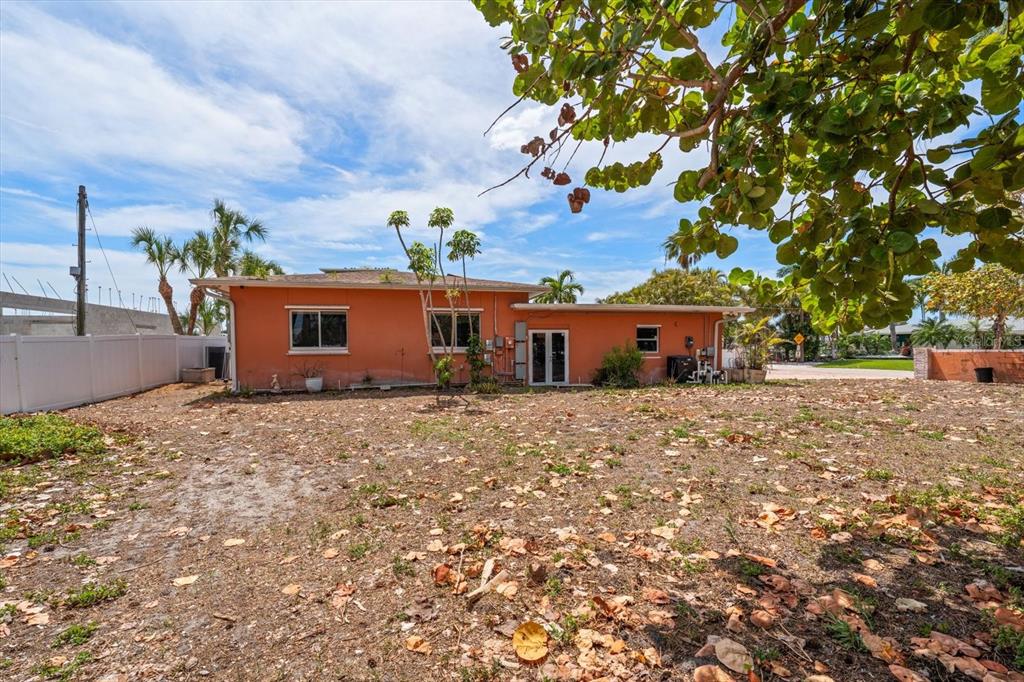 The exterior of a single-story orange house features a large, dry, leaf-covered backyard — 630-650 79TH AVENUE, ST PETE BEACH, FL