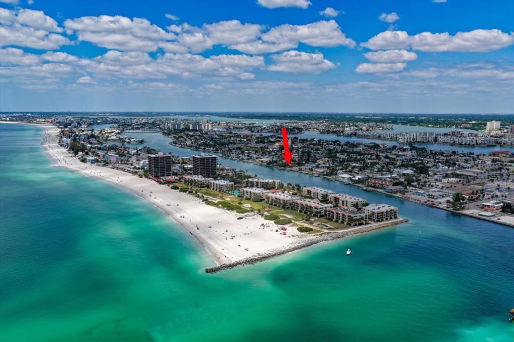 An aerial view shows a sandy beach, multi-story buildings, and a waterway with a red arrow — 630-650 79TH AVENUE, ST PETE BEACH, FL
