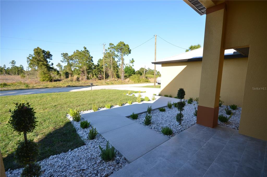 A concrete walkway leads to the front entrance of a house with a gravel garden — 1242 HATHOR STREET E, LEHIGH ACRES, FL