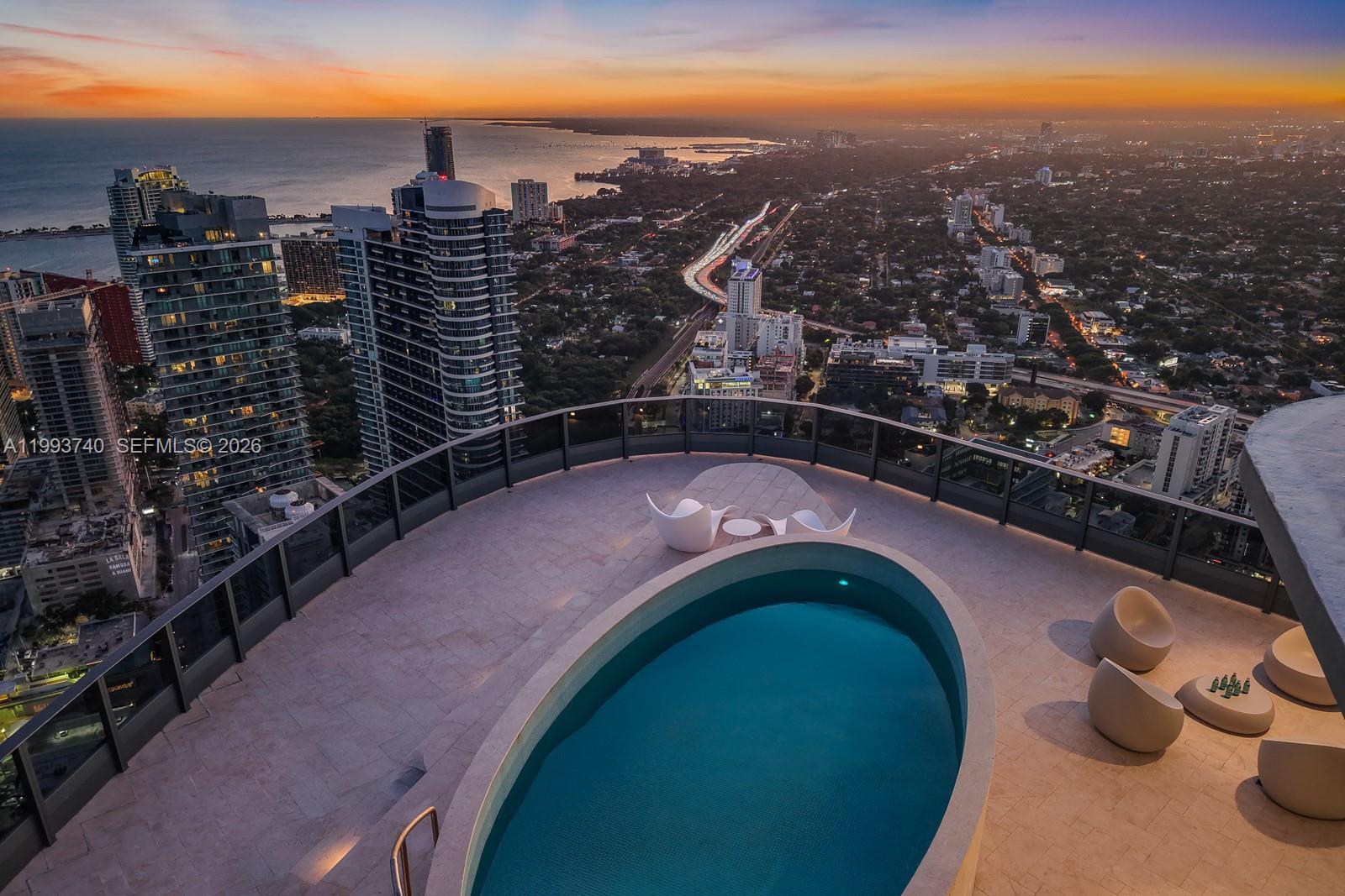 An elevated terrace features an oval swimming pool and modern seating overlooking a city skyline — 1000 Brickell Plz, Miami FL 33131, MIAMI, FL