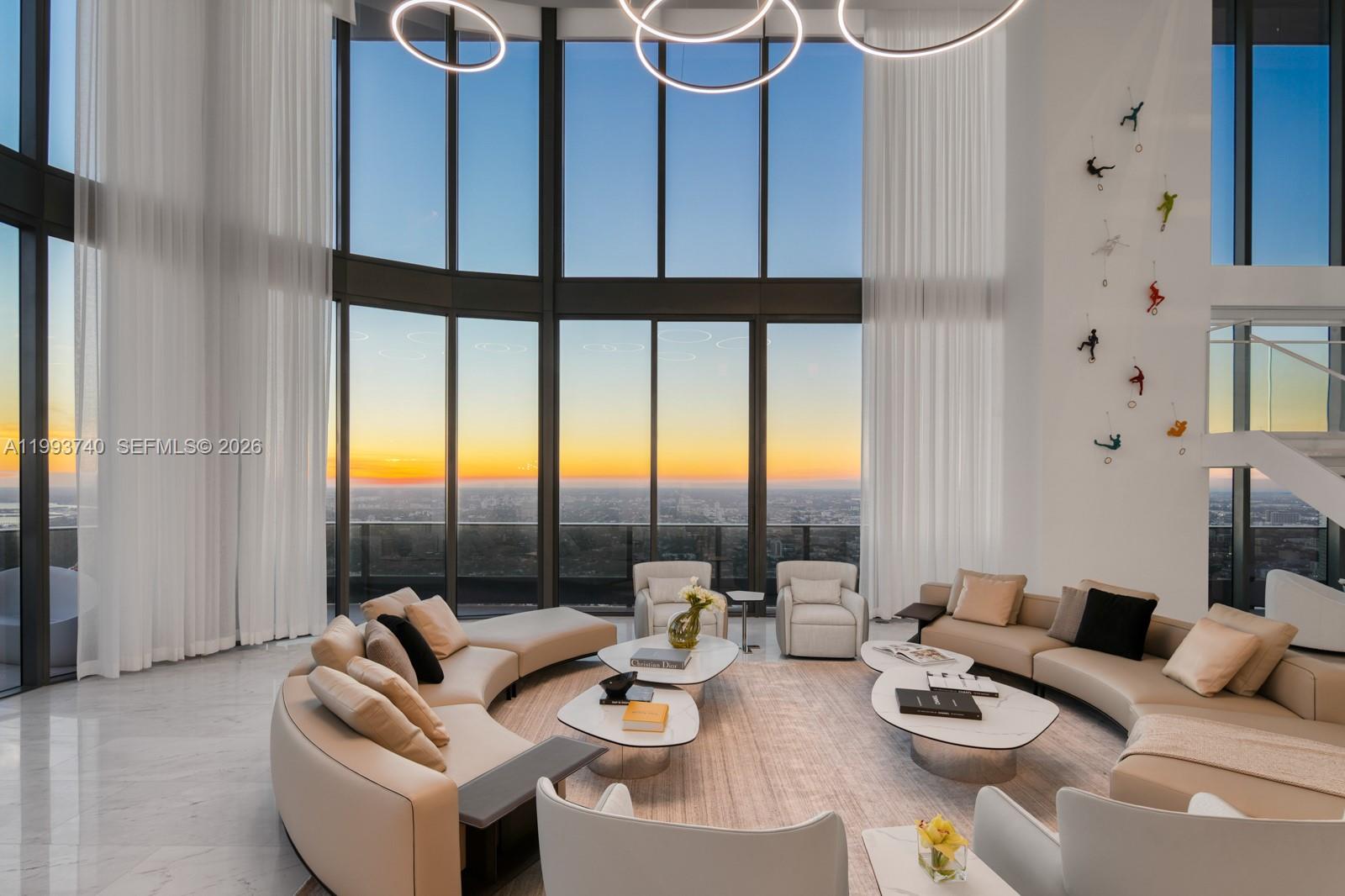 A spacious living room features floor-to-ceiling windows, curved sofas, and wall-mounted climber figurines — 1000 Brickell Plz, Miami FL 33131, MIAMI, FL