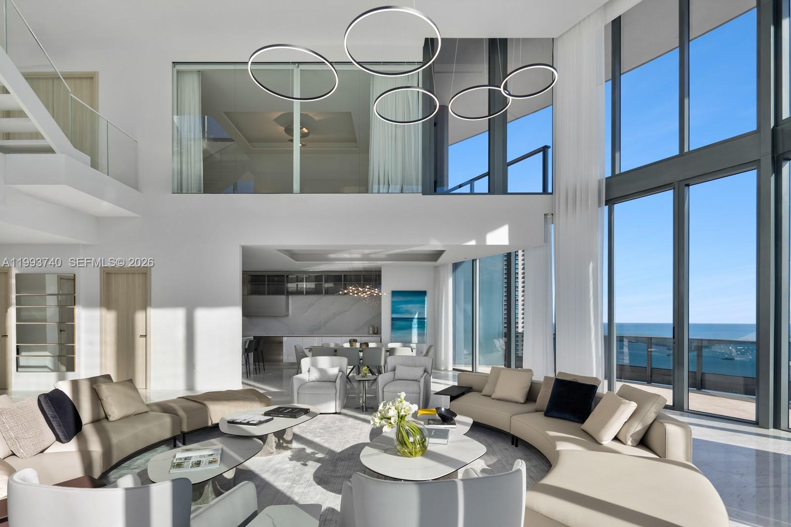 A modern, double-height living room features floor-to-ceiling windows, circular pendant lights, and ocean views — 1000 Brickell Plz, Miami FL 33131, MIAMI, FL