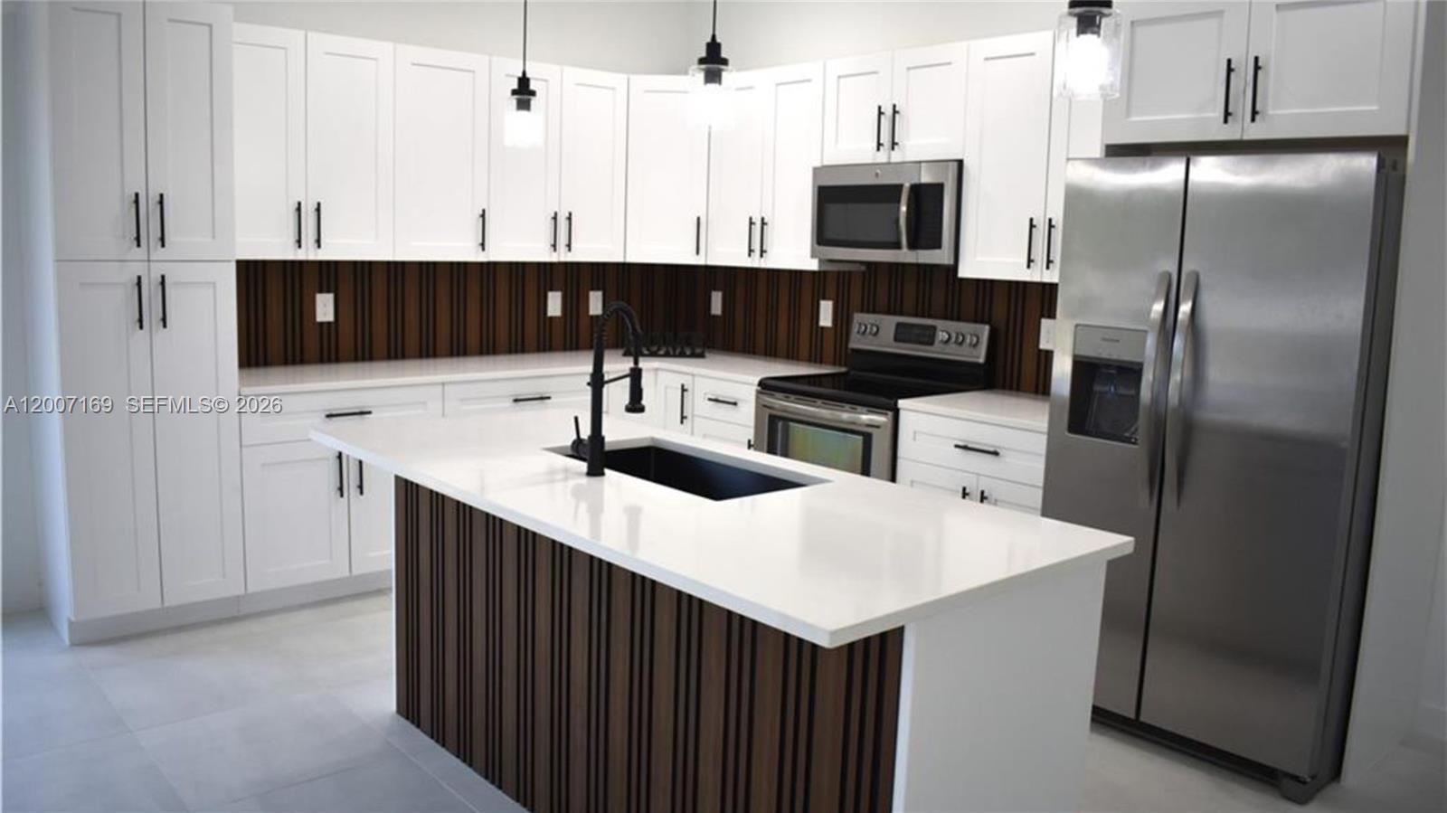 A modern kitchen features white cabinets, a wood-slatted island, and stainless steel appliances — 1006 Hamilton, Lehigh Acres FL 33972, LEHIGH ACRES, FL