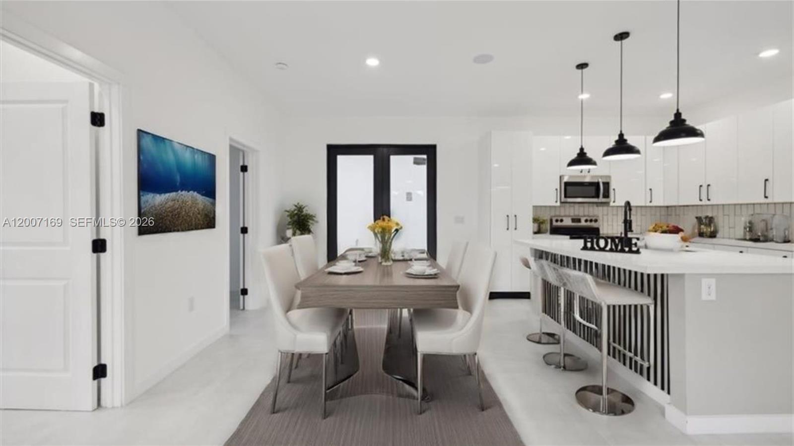 A modern dining area and kitchen with white cabinetry, a wooden table, and pendant lighting — 1006 Hamilton, Lehigh Acres FL 33972, LEHIGH ACRES, FL