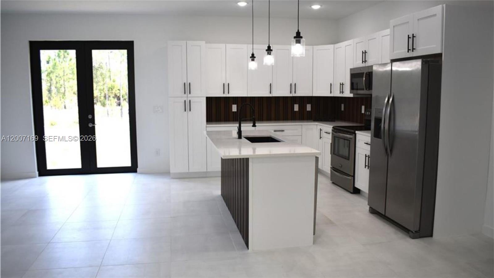 A modern kitchen features white cabinets, a dark wood-paneled island, and stainless steel appliances — 1006 Hamilton, Lehigh Acres FL 33972, LEHIGH ACRES, FL