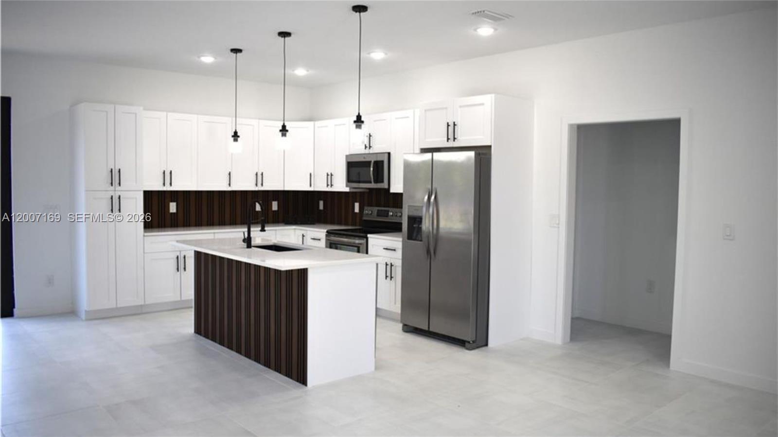 A modern kitchen features white cabinets, a dark wood-paneled island, and stainless steel appliances — 1006 Hamilton, Lehigh Acres FL 33972, LEHIGH ACRES, FL