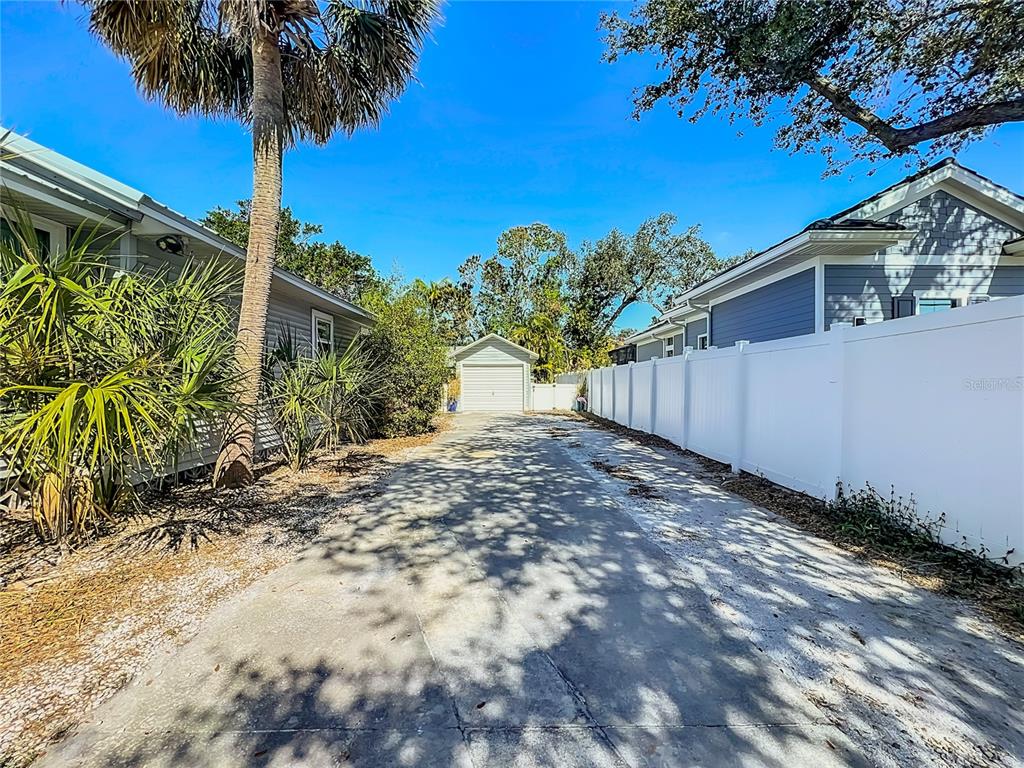 A concrete driveway leads to a detached garage between two houses with a white fence — 1687 ARLINGTON STREET, SARASOTA, FL