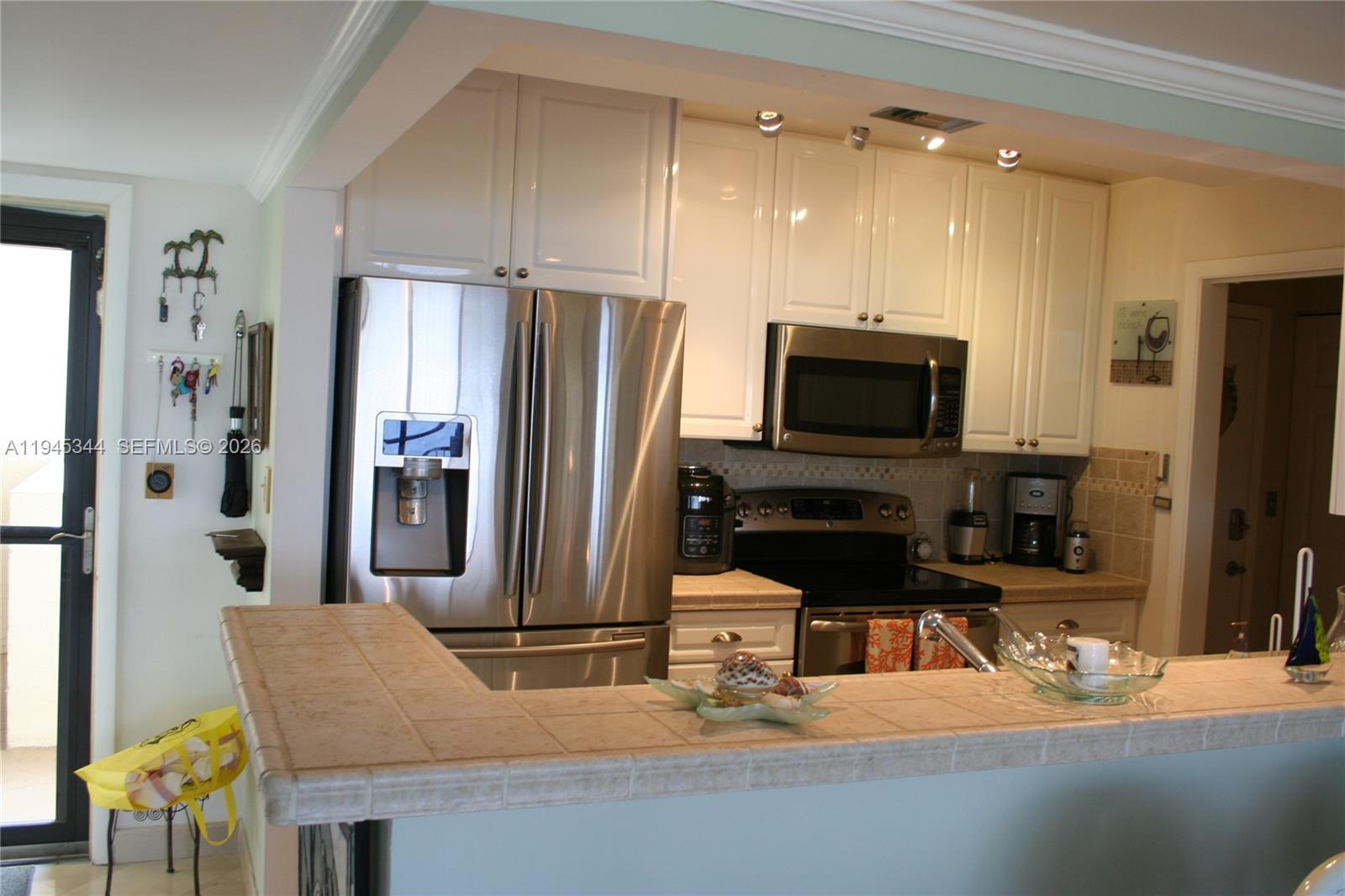 A kitchen features white cabinets, stainless steel appliances, and a tiled breakfast bar counter — 104500 Overseas Hwy # A302, Key Largo FL 33037, KEY LARGO, FL
