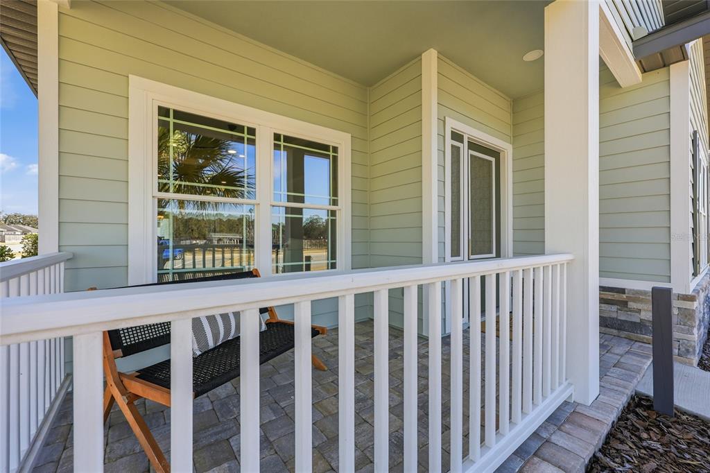 A covered front porch with light green siding, white railings, and a stone-accented exterior wall — 9567 SW 66TH LANE, GAINESVILLE, FL