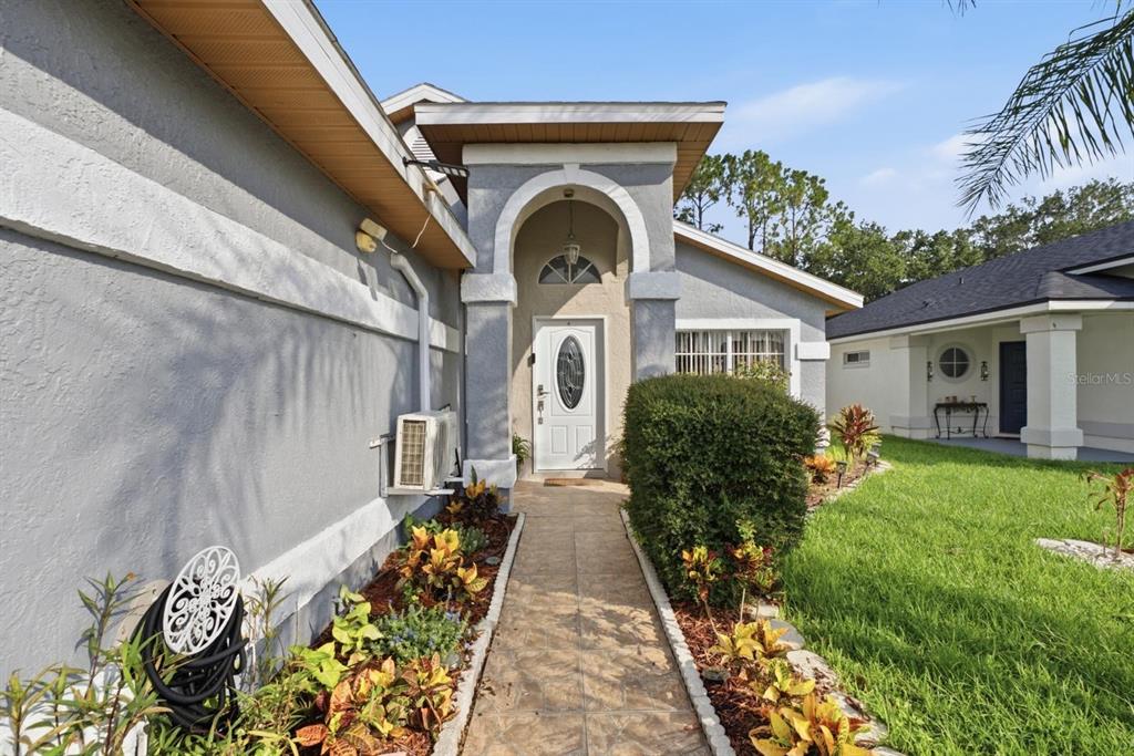 A paved walkway leads to the front entrance of a gray house with an arched porch — 2976 STILLWATER DRIVE, KISSIMMEE, FL