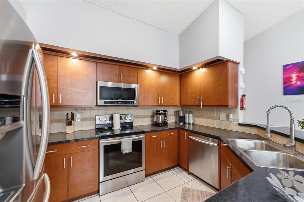 A kitchen features wood cabinets, stainless steel appliances, dark countertops, and a double basin sink — 2976 STILLWATER DRIVE, KISSIMMEE, FL