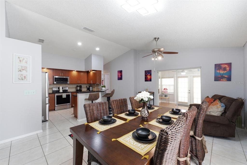 A dining area with a wooden table and wicker chairs opens to a kitchen and living room — 2976 STILLWATER DRIVE, KISSIMMEE, FL