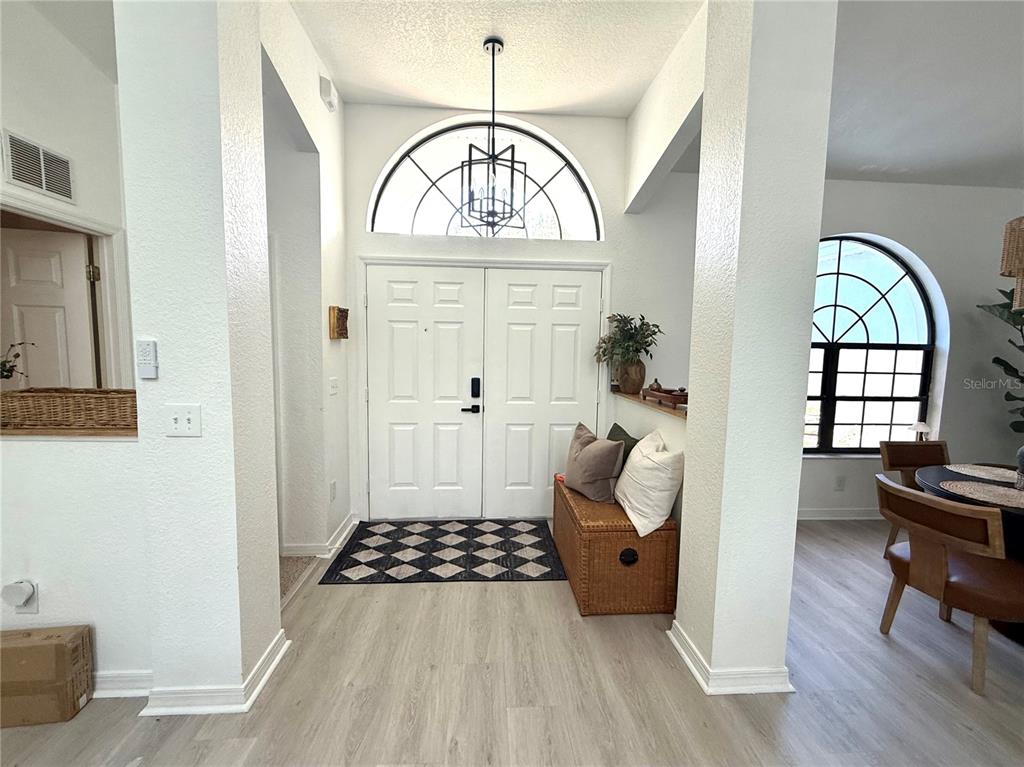 A bright entryway features double doors, a large arched window, a chandelier, and light wood flooring — 10195 SW 132ND AVENUE, DUNNELLON, FL