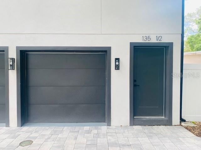 A modern exterior view shows a garage door and a side entry door with lighting — 135 48TH AVENUE N UNIT B, ST PETERSBURG, FL