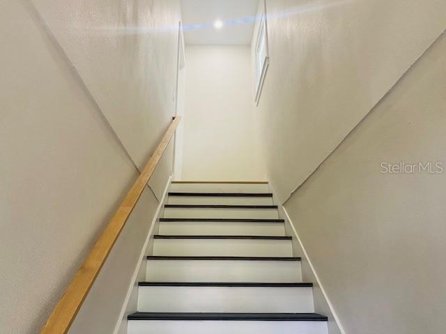 A staircase with white risers, dark treads, and a wooden handrail leads upward — 135 48TH AVENUE N UNIT B, ST PETERSBURG, FL
