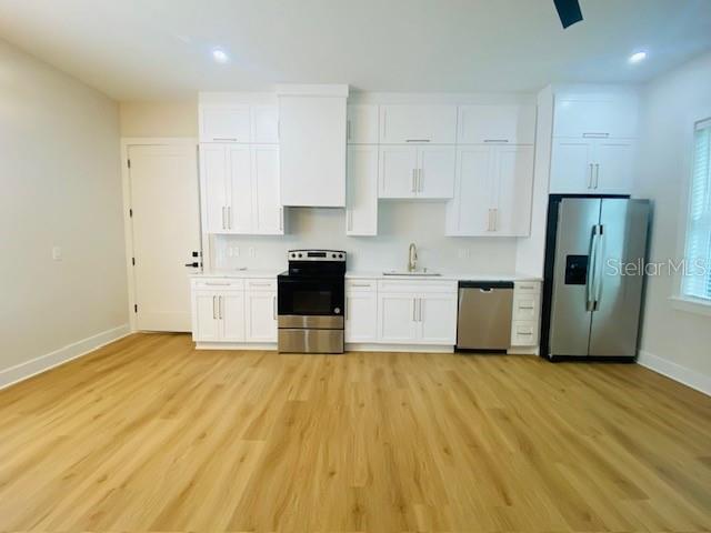 A modern kitchen features white cabinetry, stainless steel appliances, and light wood-look flooring — 135 48TH AVENUE N UNIT B, ST PETERSBURG, FL