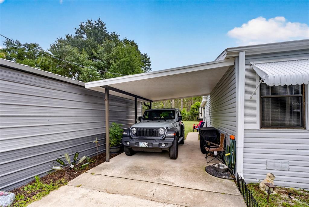 A gray Jeep is parked under a metal carport between two light-colored siding structures — 18544 SE 55TH PLACE, OCKLAWAHA, FL