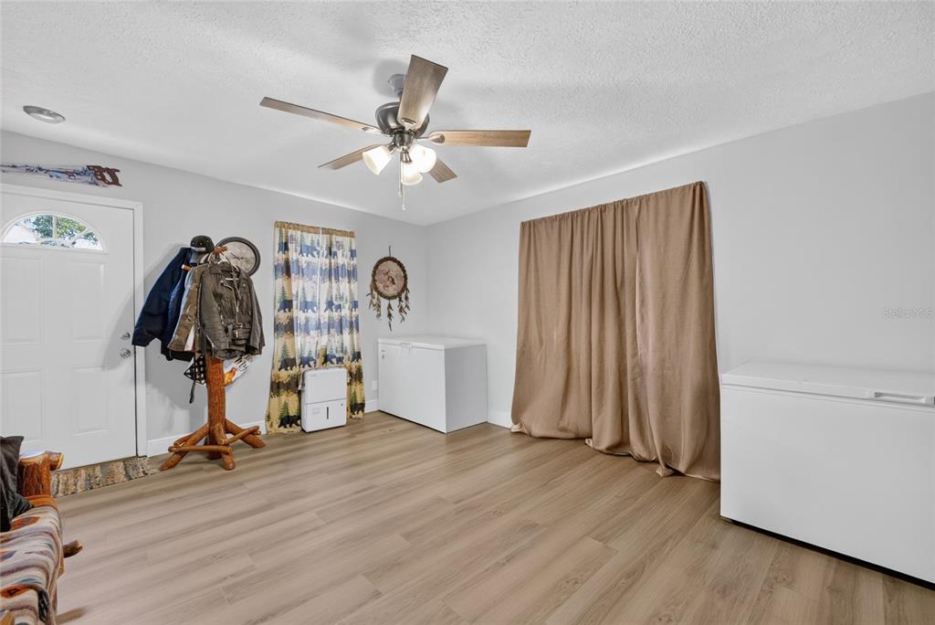 A room with light wood-look flooring, a ceiling fan, two chest freezers, and a coat rack — 18544 SE 55TH PLACE, OCKLAWAHA, FL
