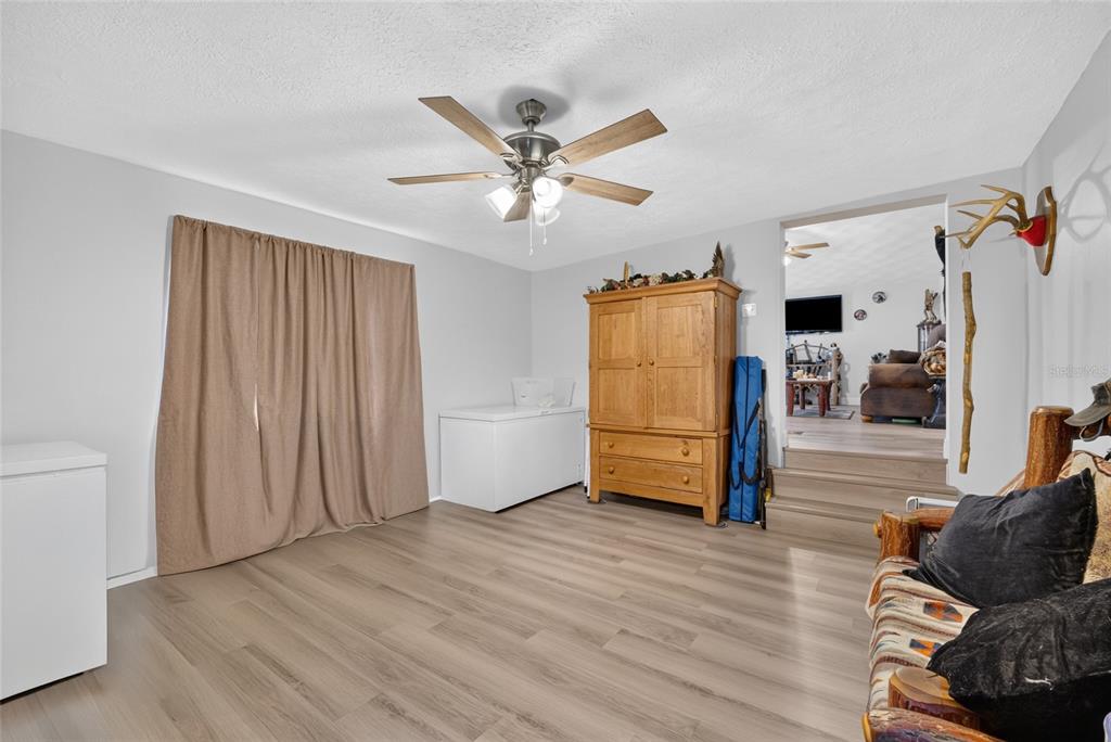 A room with light wood-look flooring, a ceiling fan, a wooden armoire, and two freezers — 18544 SE 55TH PLACE, OCKLAWAHA, FL