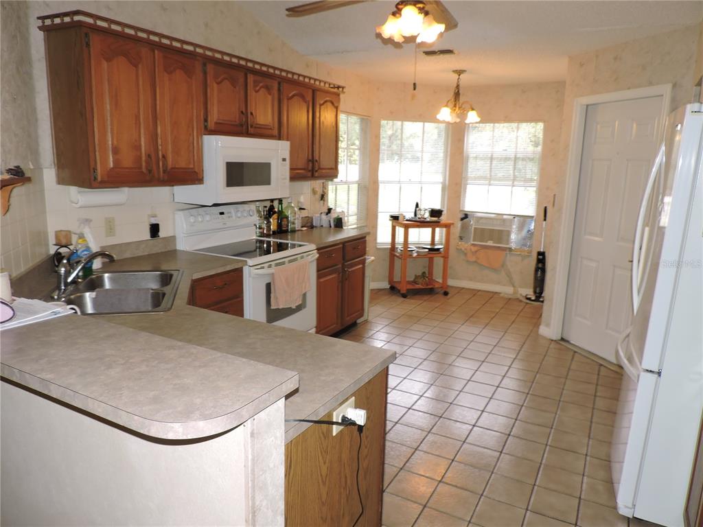 A kitchen features wood cabinets, white appliances, a double sink, and tiled flooring — 5324 FAIRMONT ROAD, LAKE WALES, FL