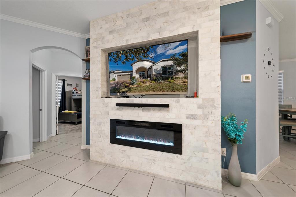 A living room features a stone-tiled fireplace wall with a mounted television and electric insert — 5396 CARRARA COURT, ST CLOUD, FL