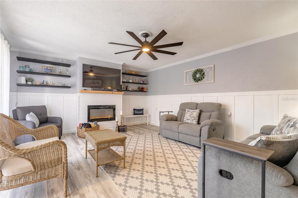 A living room features a fireplace, gray furniture, a wicker chair, and white wainscoting — 178 MOONSTONE COURT, PORT ORANGE, FL