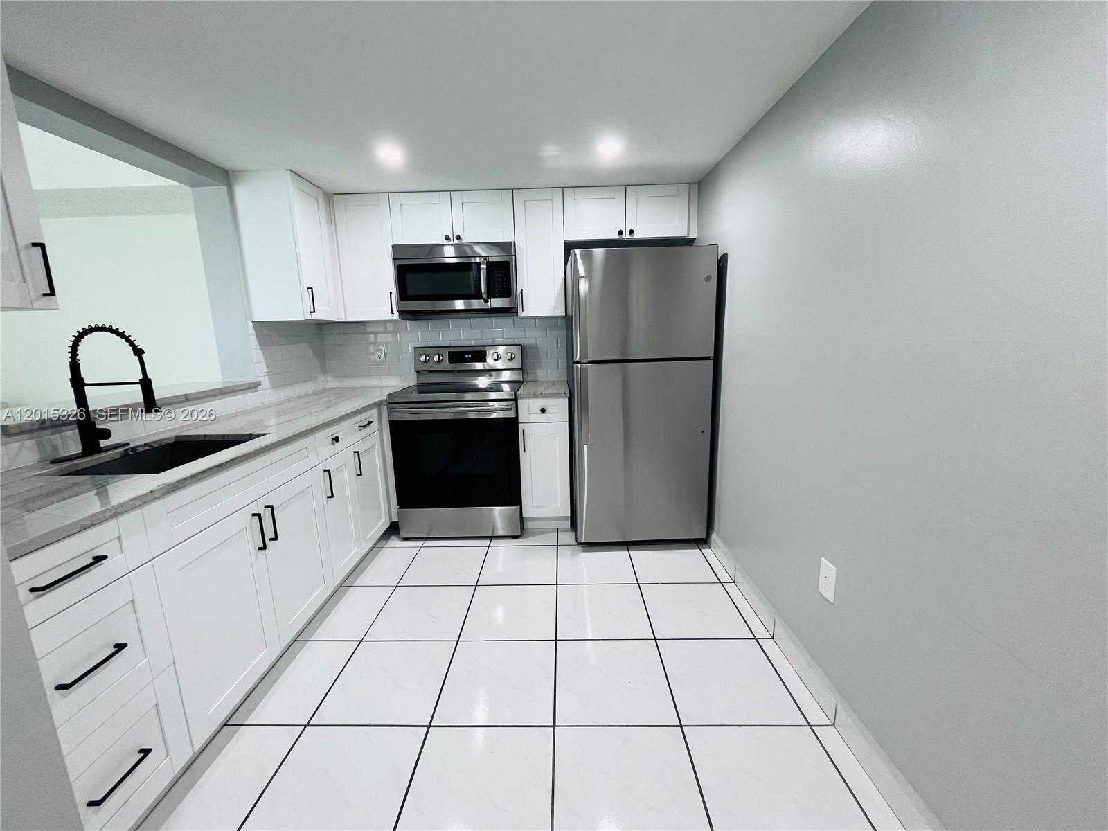 A kitchen features white cabinets, stainless steel appliances, a black faucet, and white tiled floors — 2055 SW 122nd Ave # 507, Miami FL 33175, MIAMI, FL