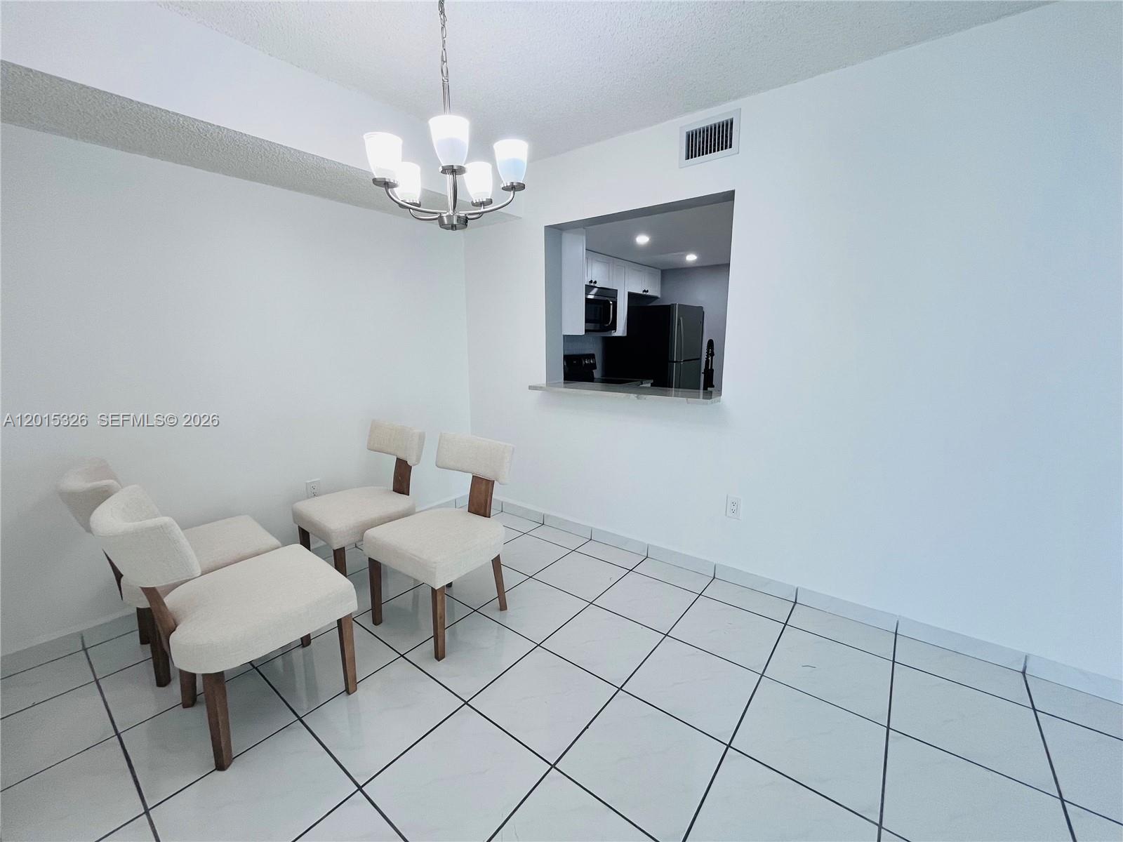 A dining area features white tile floors, a chandelier, and a pass-through to the kitchen — 2055 SW 122nd Ave # 507, Miami FL 33175, MIAMI, FL