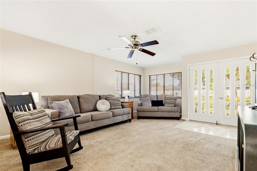 A living room features gray sofas, a dark rocking chair, carpeted floors, and a ceiling fan — 8 LLADD COURT, PALM COAST, FL