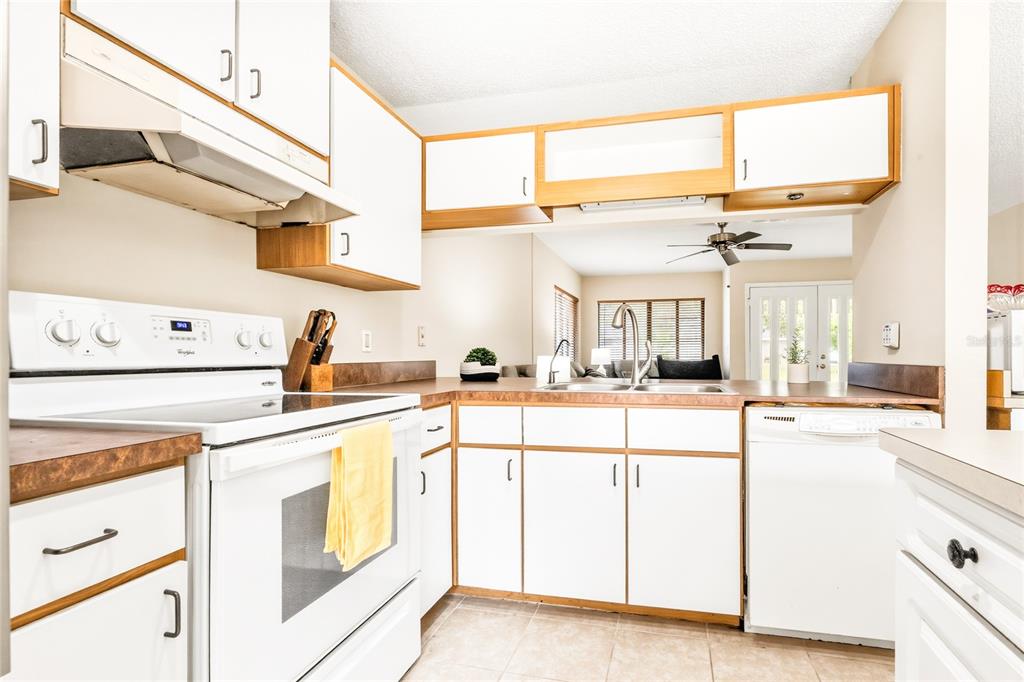 A kitchen features white cabinets, a white stove, a dishwasher, and a view into the living area — 8 LLADD COURT, PALM COAST, FL