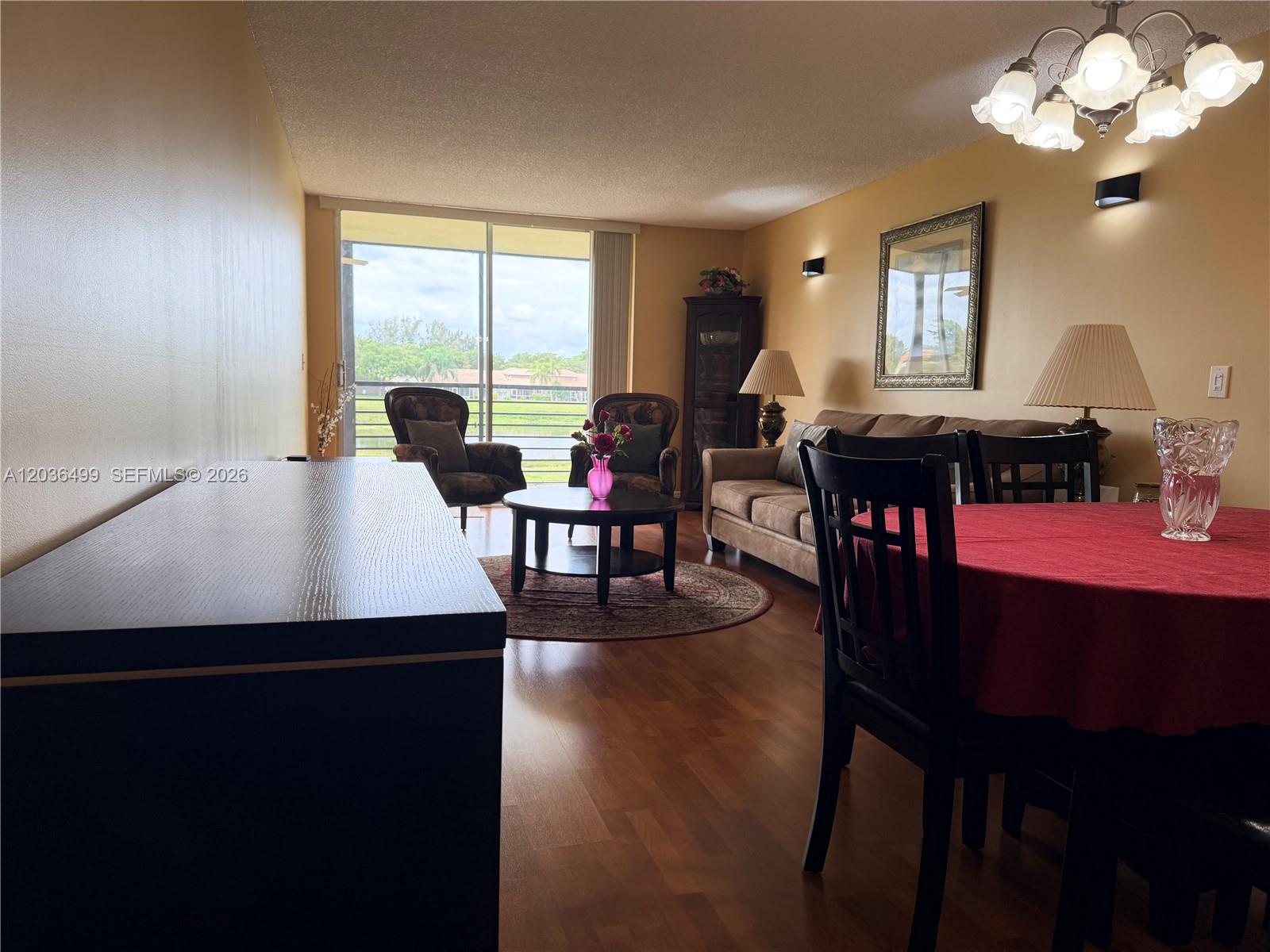 A living and dining area features wood flooring, a sliding glass door, and warm lighting — 3241 Holiday Springs Blvd # 204, Margate FL 33063, MARGATE, FL