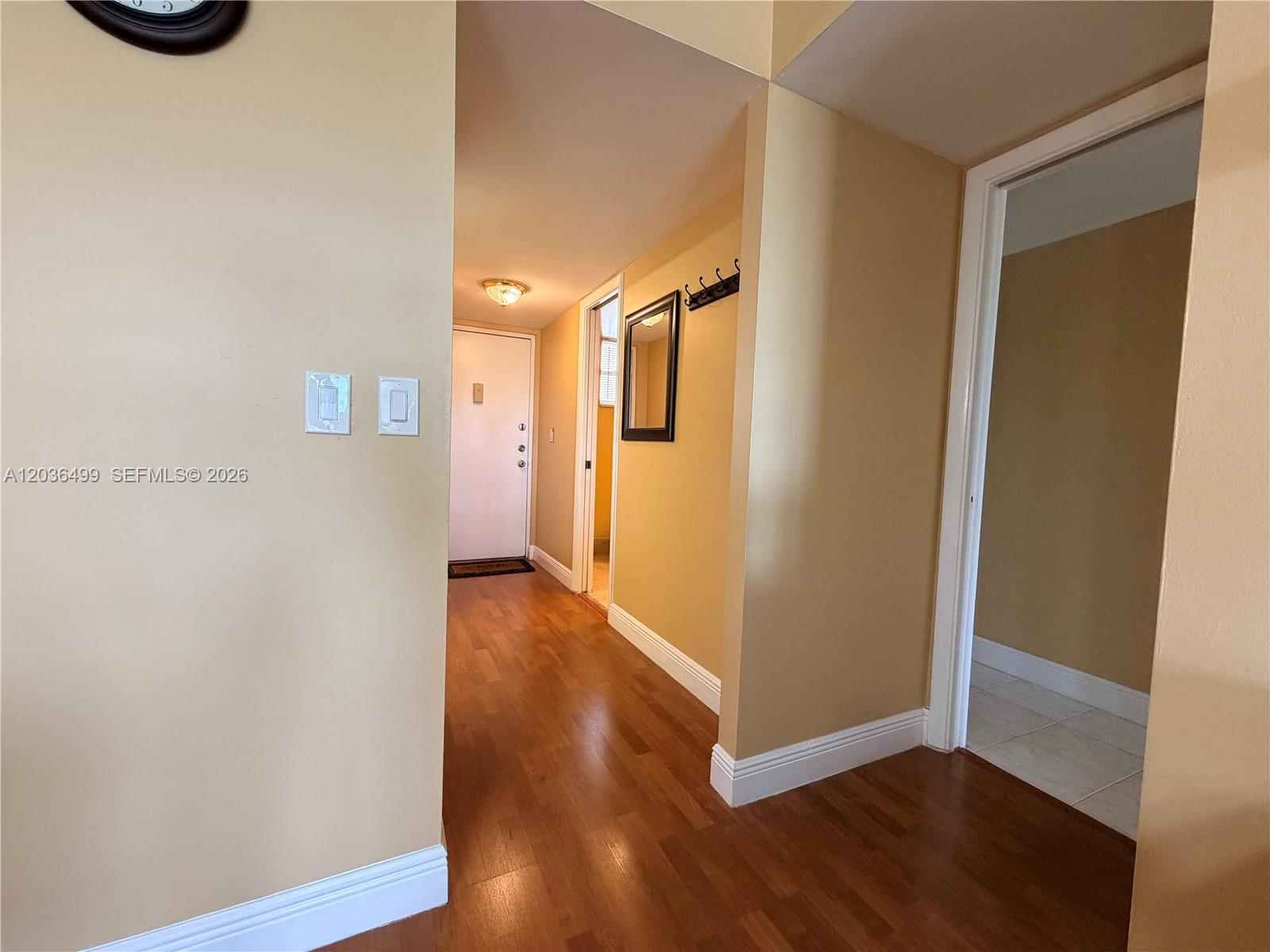 A hallway with hardwood floors leads to a white door and an adjacent room — 3241 Holiday Springs Blvd # 204, Margate FL 33063, MARGATE, FL