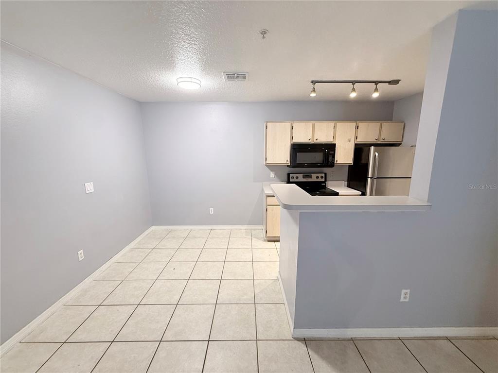 A kitchen with light wood cabinets and a breakfast bar opens to a tiled dining area — 4328 S KIRKMAN ROAD UNIT 1303, ORLANDO, FL