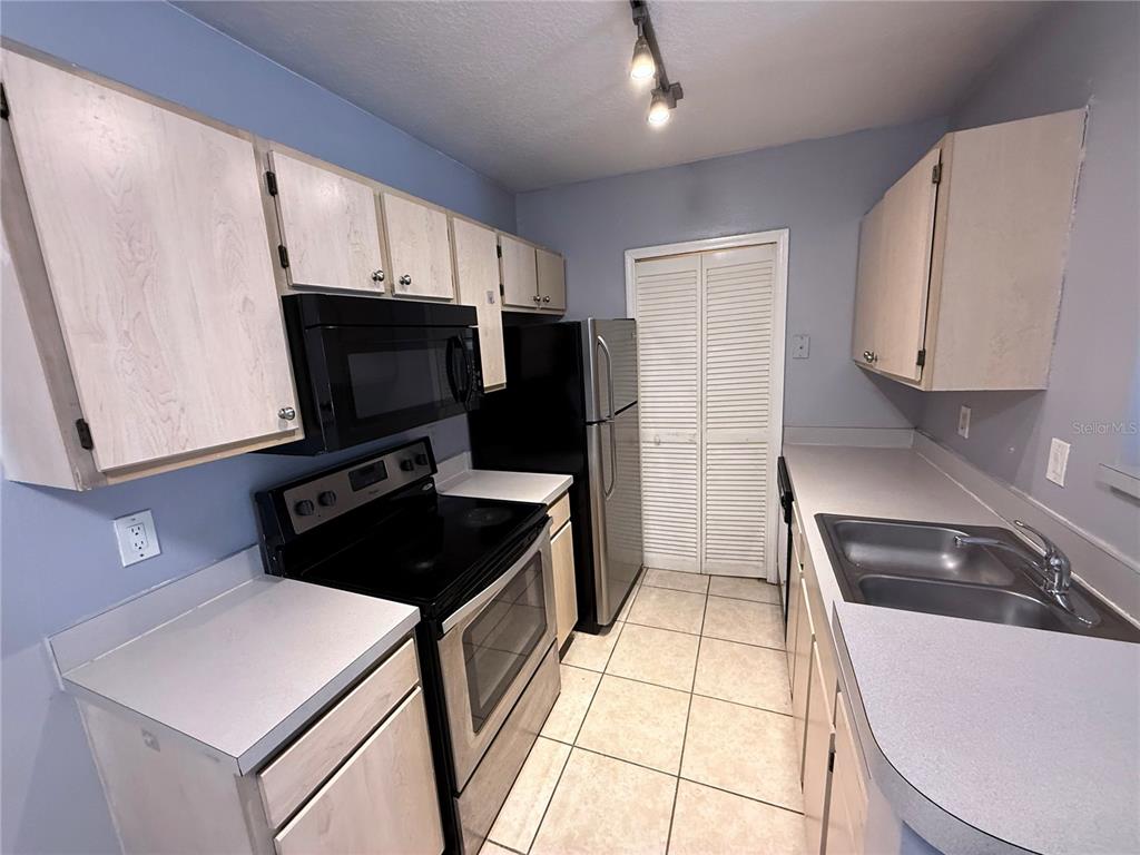 A kitchen features light-colored cabinets, black appliances, a stainless steel refrigerator, and tiled flooring — 4328 S KIRKMAN ROAD UNIT 1303, ORLANDO, FL